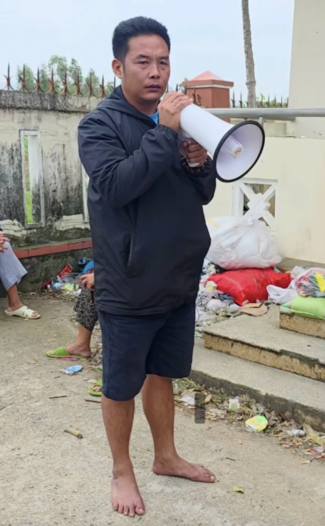 Anh Phạm Văn Long, 42 tuổi, trưởng thôn Mỹ Phú 1, xã Ô Loan, tỉnh Đăk Lăk đi chân đất, đọc tên từng người dân lên nhận quà của đoàn từ thiện hôm 28/11. Ảnh: Thi Tourguide