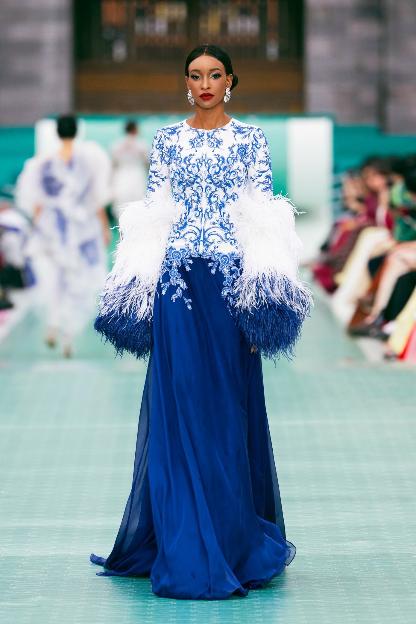 NTK Lê Thanh Hòa khéo léo chuyển tải hình ảnh tường thành rêu phong, mái ngói cổ kính, khung cửa chạm rồng phượng, cùng các giá trị thủ công truyền thống: Sơn mài, Pháp lam, thêu cung đình, tranh kính, hay trang phục truyền thống như áo Ngũ Thân, Nhật Bình. Tất cả được tái hiện qua kỹ thuật hiện đại, tạo nên một khúc giao hưởng đặc biệt giữa di sản và phong cách đương đại.