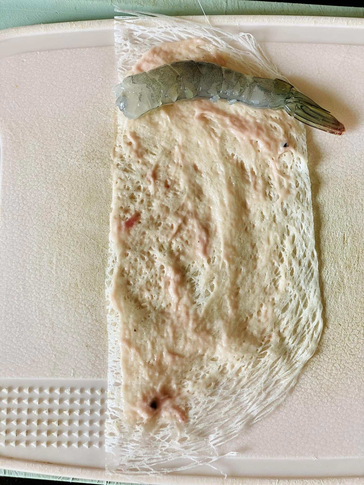 Cắt đôi bánh cuốn rế rồi phết 1 lớp mỏng giò sống lên trên, lần lượt cuộn quanh mình tôm cho đến hết.