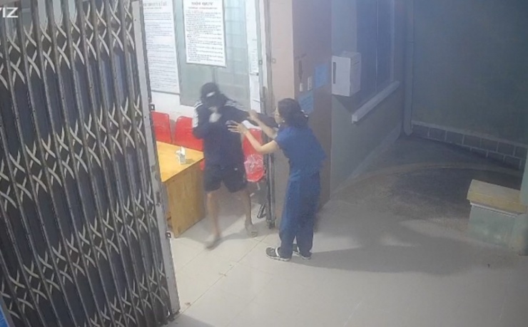 Nữ nhân viên y tế tìm cách thoát ra ngoài nhưng đã bị kẻ cướp túm cổ áo, cầm dao không chế, đe dọa tính mạng.
