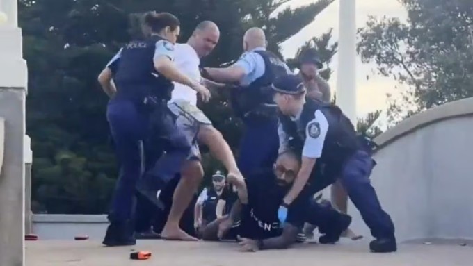 Cảnh sát Australia cố tách đám đông giận dữ khỏi người bị nhận diện nhầm là nghi phạm xả súng ở bãi biển Bondi hôm 14/12. Ảnh: 7News