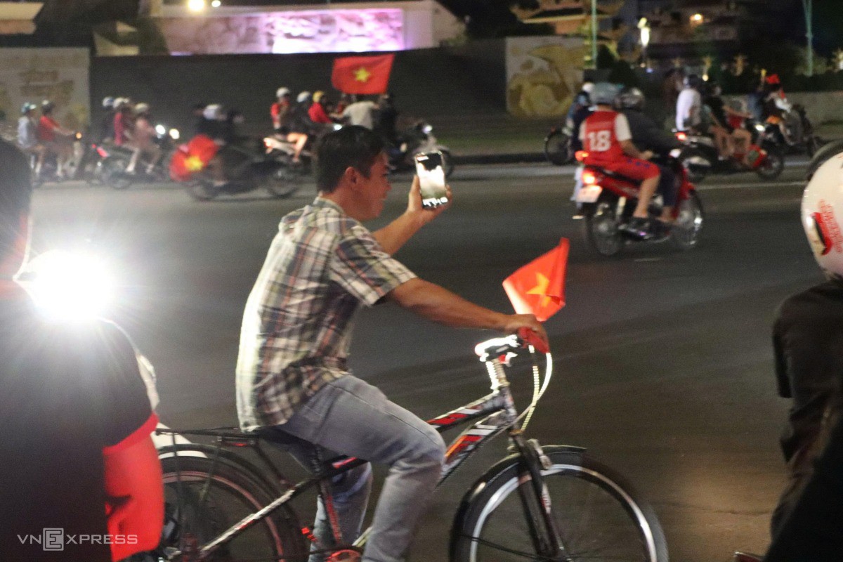 Người đàn ông ở Phan Thiết đi xe đạp vừa cầm cờ hò reo vừa tranh thủ dừng lại bên đường livestream cho bạn bè ở xa cùng xem. Ảnh: Việt Quốc