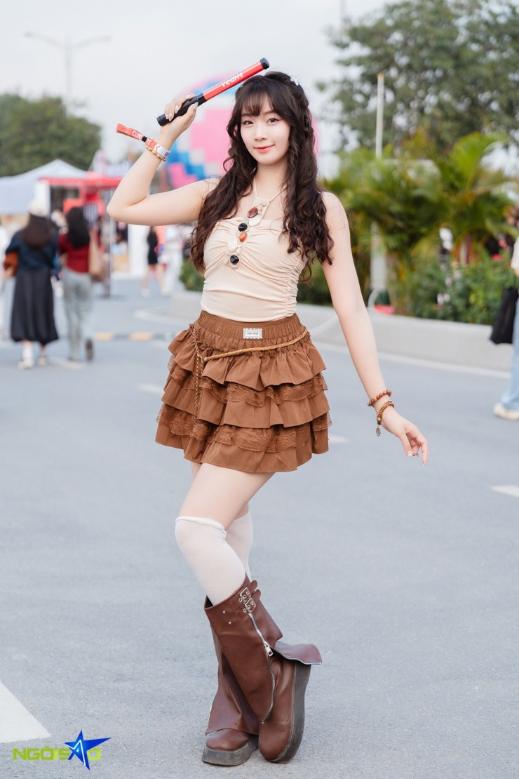 Thu Trang diện áo hai dây ôm màu be với chi tiết nhún nhẹ, tôn dáng và tạo nét mềm mại. Cô phối chân váy ngắn nhiều tầng màu nâu, bèo và ren, mang lại vẻ ngọt ngào. Tóc uốn xoăn nhẹ, để mái cùng tông nâu-be đồng điệu giúp tổng thể trông dễ thương và hài hòa.