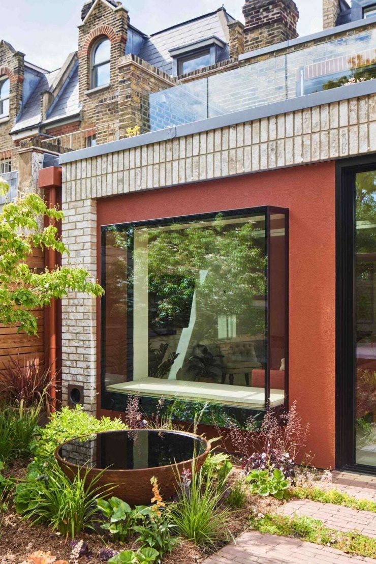 Mặt đứng phía sau của ngôi nhà nổi bật với lớp hoàn thiện màu đất đỏ và cửa sổ kính lớn. Giải pháp mở rộng về phía vườn giúp tăng diện tích sử dụng và cải thiện đáng kể khả năng lấy sáng cho tầng trệt. Nguồn: Archello