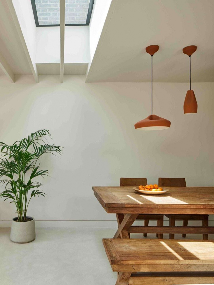 Không gian ăn uống với bàn gỗ dài đặt dưới giếng trời, ánh sáng tự nhiên chiếu trực tiếp xuống mặt bàn. Giếng trời giúp khu vực ăn uống luôn sáng và thông thoáng, giảm phụ thuộc vào đèn điện ban ngày. Nguồn: Archello