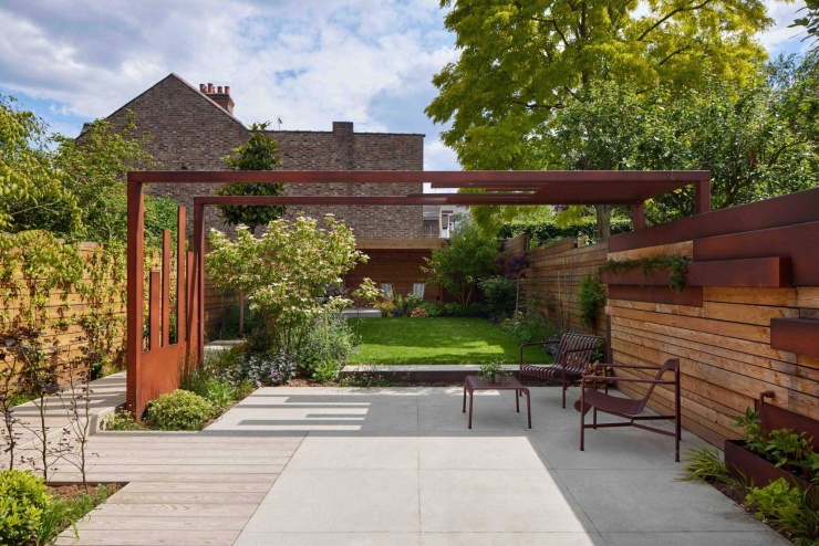 Không gian sân vườn nhìn từ trong nhà ra, nổi bật với khung thép màu russet chạy dọc khu đất. Giải pháp khung thép kết hợp cảnh quan giúp kết nối các lớp không gian và dẫn hướng tầm nhìn ra phía cuối vườn. Nguồn: Archello