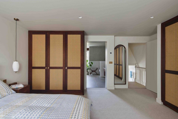 Phòng ngủ chính được bố trí tối giản với hệ tủ gỗ kết hợp mây đan, mang lại cảm giác ấm áp và thư giãn. Vật liệu tự nhiên giúp cân bằng lại các chi tiết kim loại mạnh mẽ xuất hiện ở khu vực cầu thang