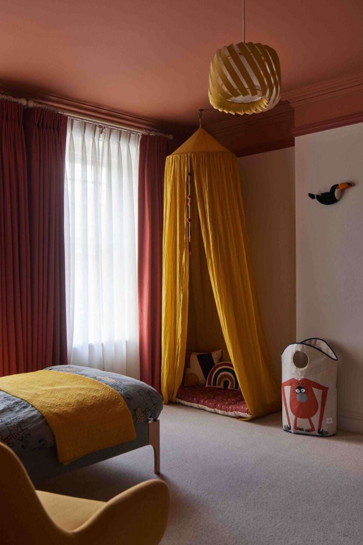 Góc vui chơi trong phòng ngủ trẻ được bố trí với lều vải và thảm ngồi sát cửa sổ. Thiết kế này tận dụng ánh sáng tự nhiên và tạo ra một không gian riêng nhỏ cho trẻ đọc sách, chơi đùa