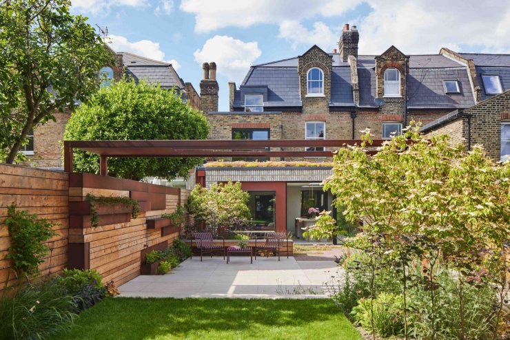 Khu vườn phía sau được tổ chức như một không gian sinh hoạt ngoài trời hoàn chỉnh, với thảm cỏ, cây xanh và lối đi rõ ràng. Hệ thép màu gỉ kết hợp hàng rào gỗ giúp định hình không gian, tạo bóng mát và tăng sự riêng tư cho khu vườn. Nguồn: Archello