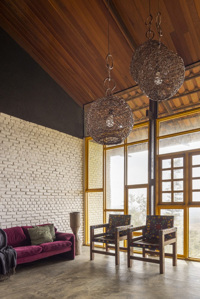 Không gian nội thất của “nhà vàng” nổi bật với tường gạch trắng sơn thô và khung cửa sơn vàng đồng bộ, tận dụng tối đa ánh sáng tự nhiên qua hệ cửa kính lớn.