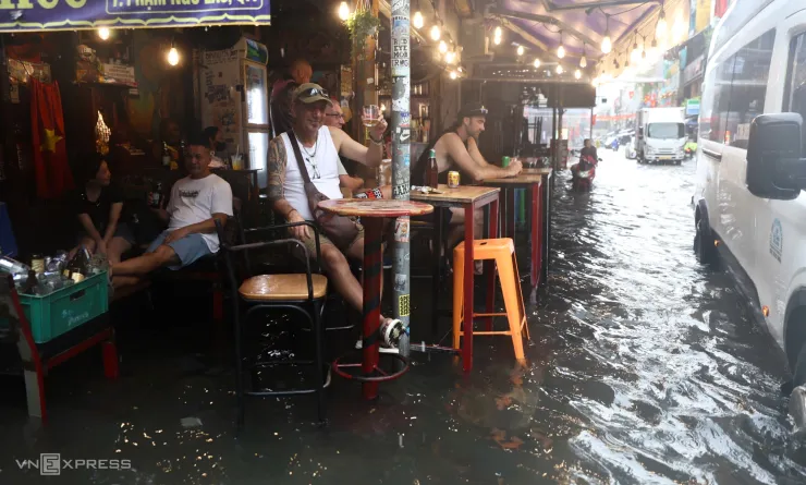 Du khách nước ngoài kê cao ghế, uống bia giữa nước ngập trên đường Bùi Viện, ngày 23/9. Ảnh: Quỳnh Trần