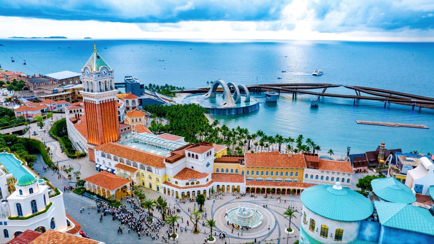 Những chiếc bánh hồng đặt cạnh tách trà hoặc cà phê, phía sau là biển và kiến trúc Địa Trung Hải của Thị trấn Hoàng Hôn, tạo nên góc check-in độc bản.